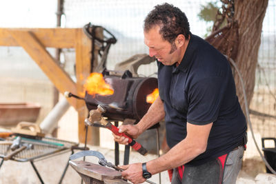 Side view of man hammering horseshoe at workshop