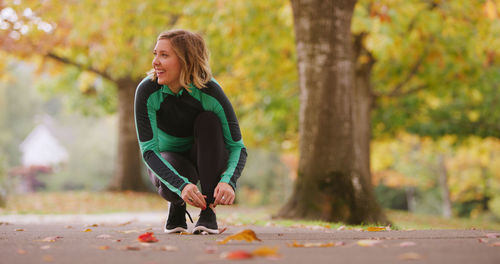 Smiling young woman tying shoelace in park during autumn