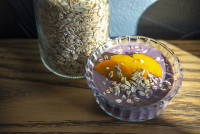 Acai smoothie, granola, fresh fruits in a glass bowl on wooden table. eating healthy breakfast bowl