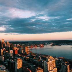 Aerial view of city at waterfront against cloudy sky