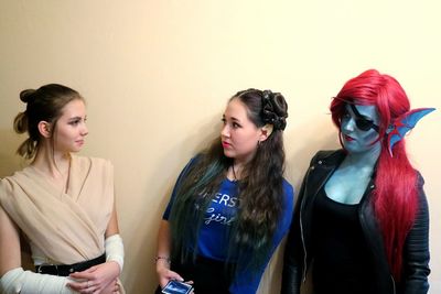 Female friends in costume talking while standing against wall