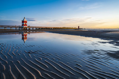 The sun rises over the calm waters of lignano sabbiadoro. explosion of colors on the red lighthouse.