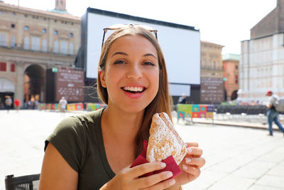 Portrait of smiling young woman holding food in city