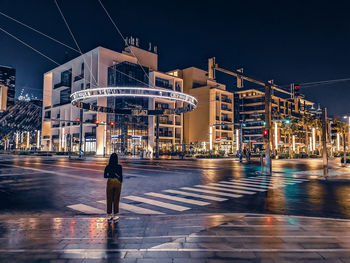 Rear view of man walking on illuminated street at night