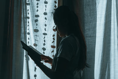 Side view of woman standing by window at home