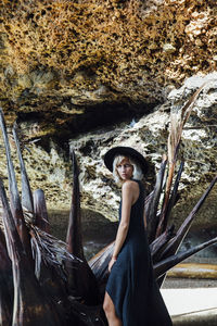 Side view portrait of young woman on driftwood against rock formation