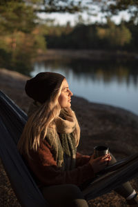 Young woman with eyes closed holding coffee cup while sitting on hammock