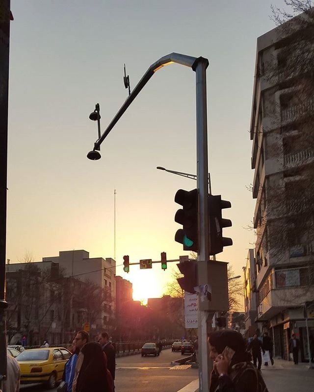 building exterior, architecture, built structure, car, city, street, transportation, land vehicle, street light, city life, mode of transport, sunset, city street, sky, road, clear sky, incidental people, sunlight, traffic