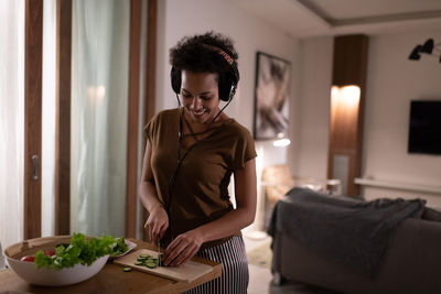 Ethnic lady cutting vegetable and listening to music