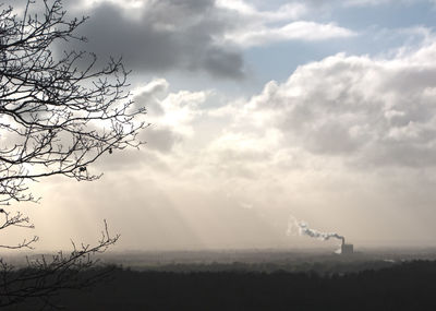 Low angle view of bare trees against cloudy sky