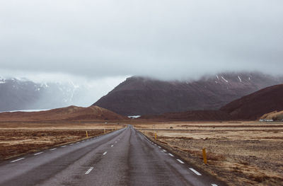 Empty road along mountain range against sky