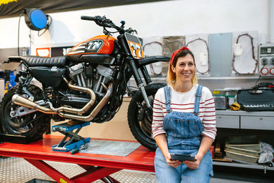 Mechanic woman holding digital tablet sitting over platform