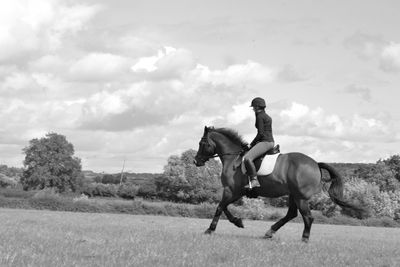 Female jockey riding horse in grassy field against sky