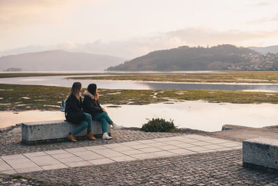 Rear view of woman sitting on retaining wall by lake