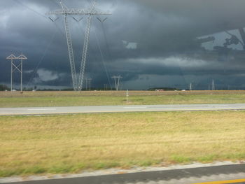 Road passing through field against cloudy sky