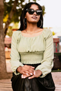 Portrait of a young woman wearing light green blouse, black skirt and sunglasses and hoop earrings