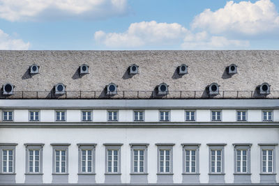 The large roof is covered with the flat tiles of the old house with many round windows in the attic