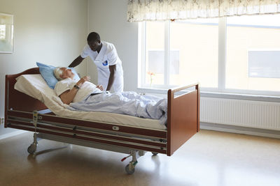 Male nurse adjusting senior man's bed in hospital ward