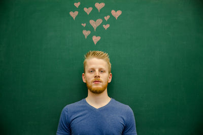 Portrait of smiling young man gesturing with heart shapes on blackboard