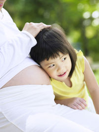 Smiling girl keeping head on abdomen of pregnant mother