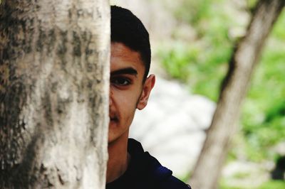 Cropped portrait of young man hiding behind tree trunk