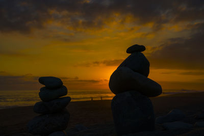 Silhouette man standing on rock at beach against sky during sunset