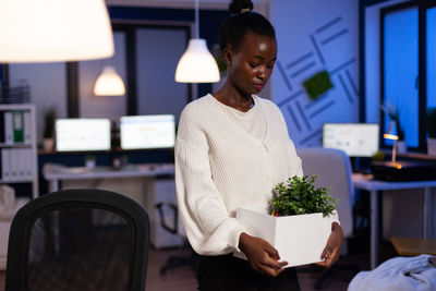 Young woman holding plant at home