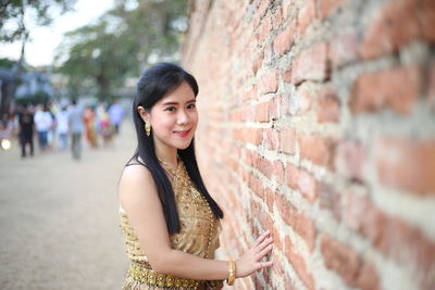 Portrait of smiling woman wearing traditional clothing standing by brick wall