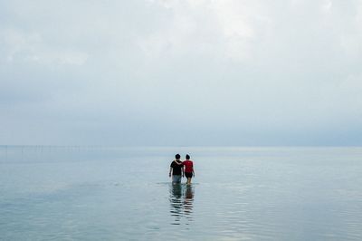 Rear view of people walking in sea against clear sky