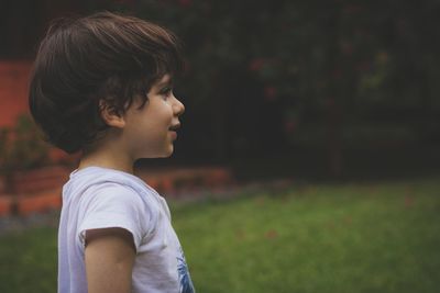 Side view of cute smiling boy looking away while standing on field