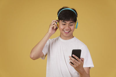 Portrait of smiling young man using smart phone against yellow background