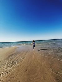 Full length of man on beach against clear blue sky