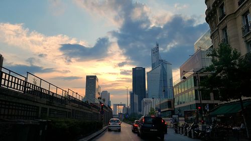 Cars on road amidst buildings in city against sky during sunset