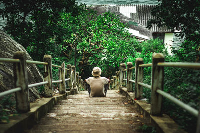 Rear view of woman sitting on footbridge against building