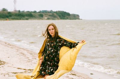 Portrait of woman holding scarf while standing on beach