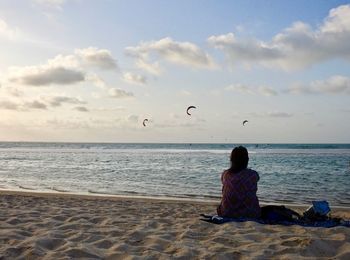 Rear view of woman sitting at beach against sky