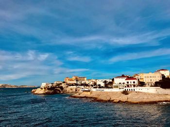 Buildings by sea against blue sky