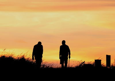 Silhouette men standing against orange sky