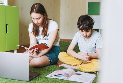 Siblings brother sister teenager and tween boy  writing in pupil book with opened laptop 