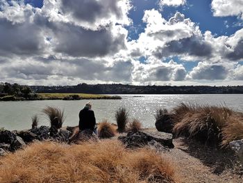 Rear view of people standing on shore against sky