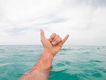 Close-up of hand over sea against sky