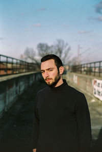 Portrait of man on footbridge against sky in city