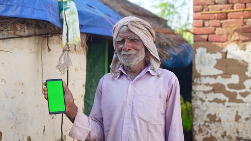 Old asian man smiling and showing a green screen cell phone with rural village life concept backgrou