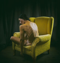 Woman sitting showing her naked back in a yellow armchair