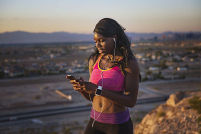 Smiling sportswoman listening music against village