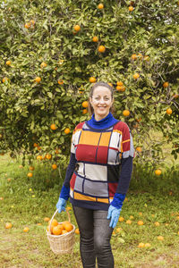 Portrait of smiling woman standing by apples on plant