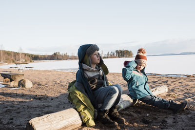 Kids sitting on a log by a frozen lake in sweden