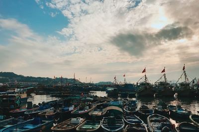 Boats moored at harbor against cloudy sky