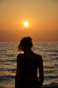 Rear view of woman looking at sea during sunset