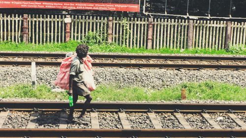 Side view of homeless man walking on railroad track with sack